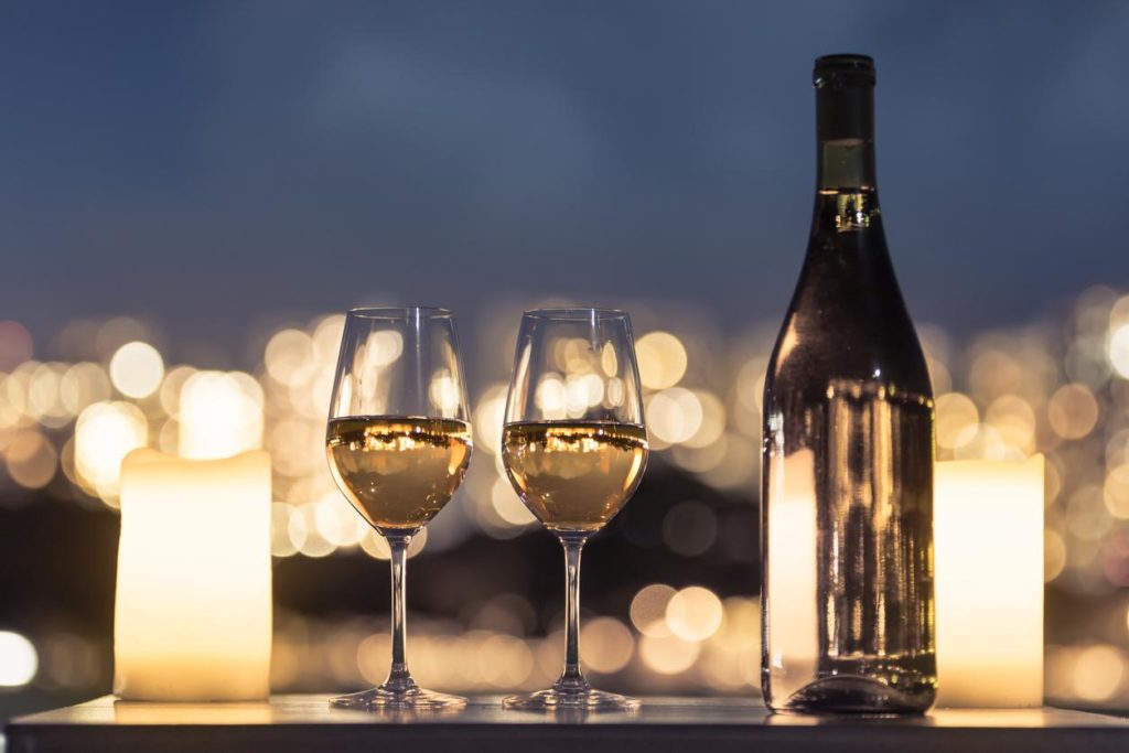 Close up of wine bottle and two glasses of wine on table outside with candles