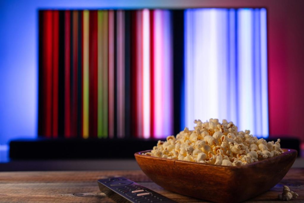 Detail of popcorn in wood bowl on table with remote and tv screen in background