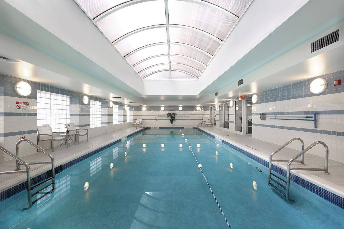 Large pool with partial arced windowed ceiling, lap lane and tiled walls with lighting at 150 East 57th Street