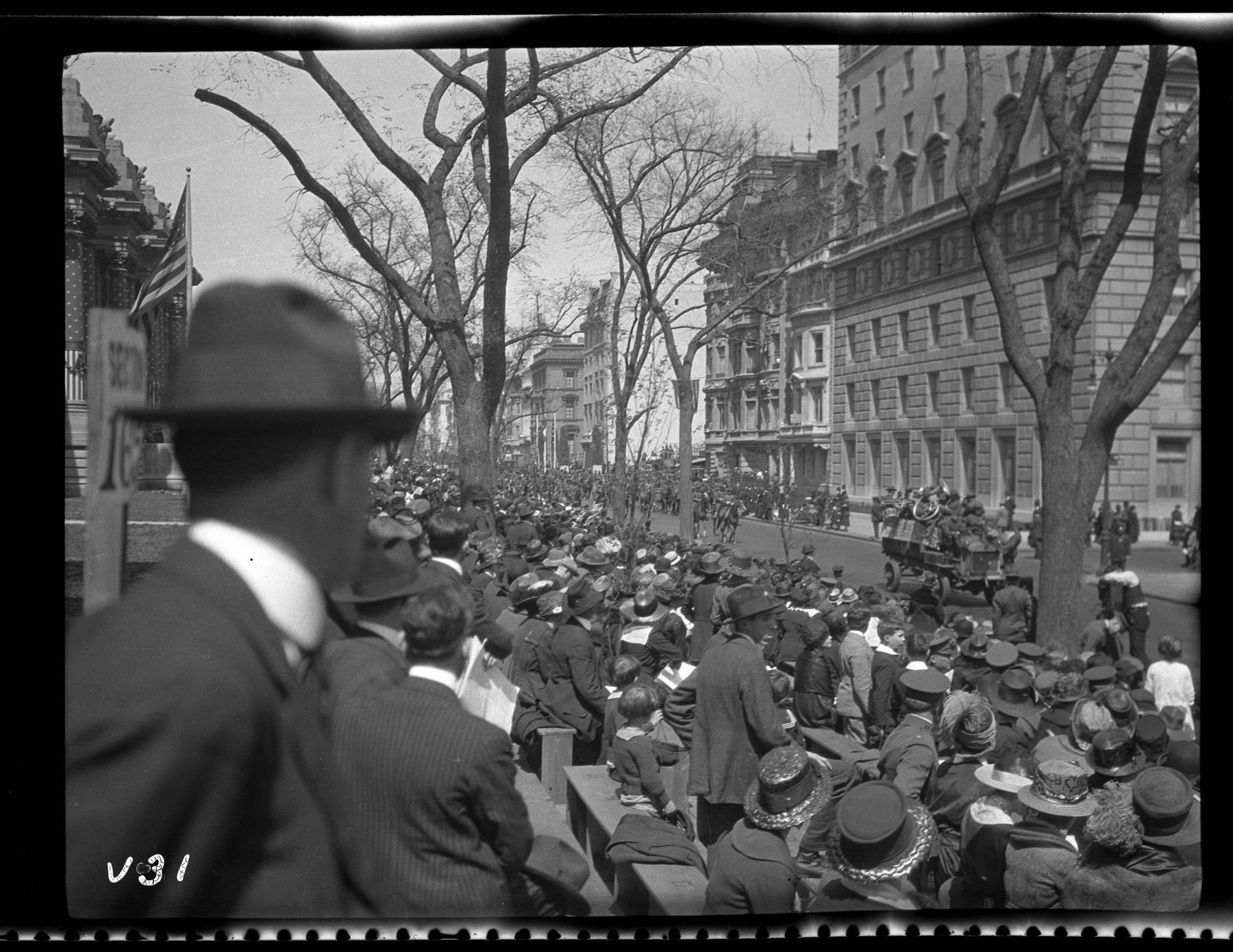 b&w photo of large group of people standing and sitting outside watching fifth ave and 80th street parade
