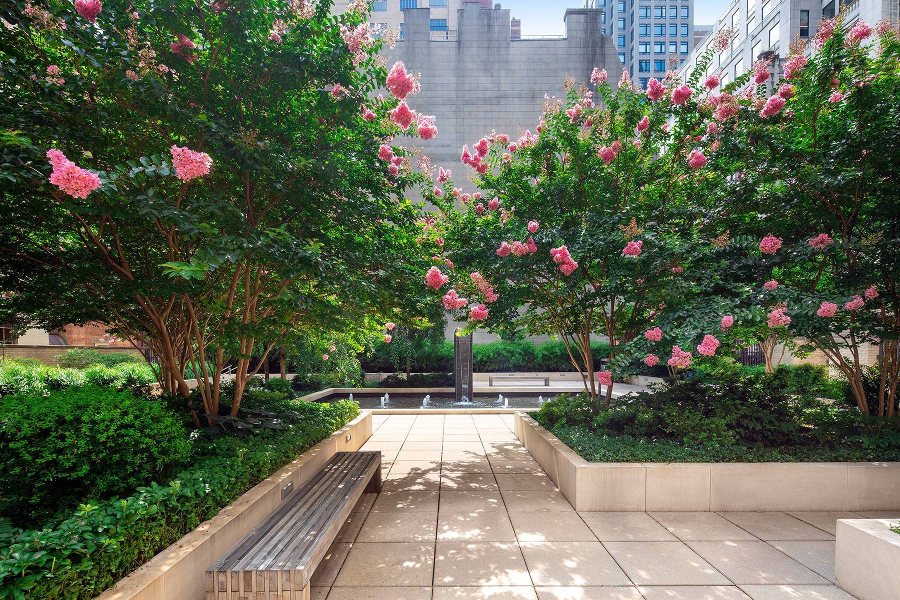 Private Landscaped Garden at 800 Fifth Avenue with trees, pink flowers, seating and a fountain